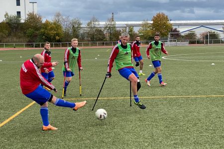 Zwei amputierte Fußballer auf Krücken im Zweikampf um den Ball auf Kunstrasen.
