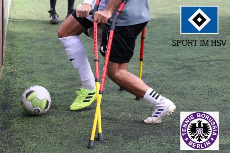 Zwei amputierte Fußballer auf Krücken im Zweikampf um den Ball auf Kunstrasen.