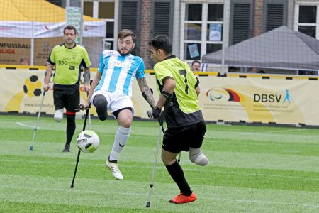 Zwei amputierte Fußballer auf Krücken im Zweikampf um den Ball auf Kunstrasen.
