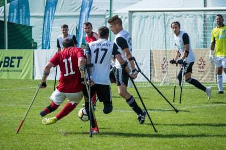 Zwei amputierte Fußballer auf Krücken im Zweikampf um den Ball auf Rasen.